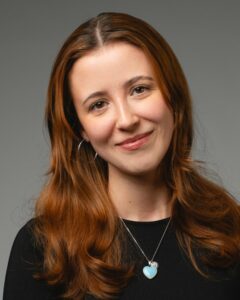 Junge Frau mit langen, braunen Haaren und schwarzem Oberteil lächelt.