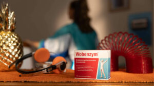 Schachtel Wobenzym steht auf Tisch, umgeben von Kopfhörern, Ananas und Plastikspirale.